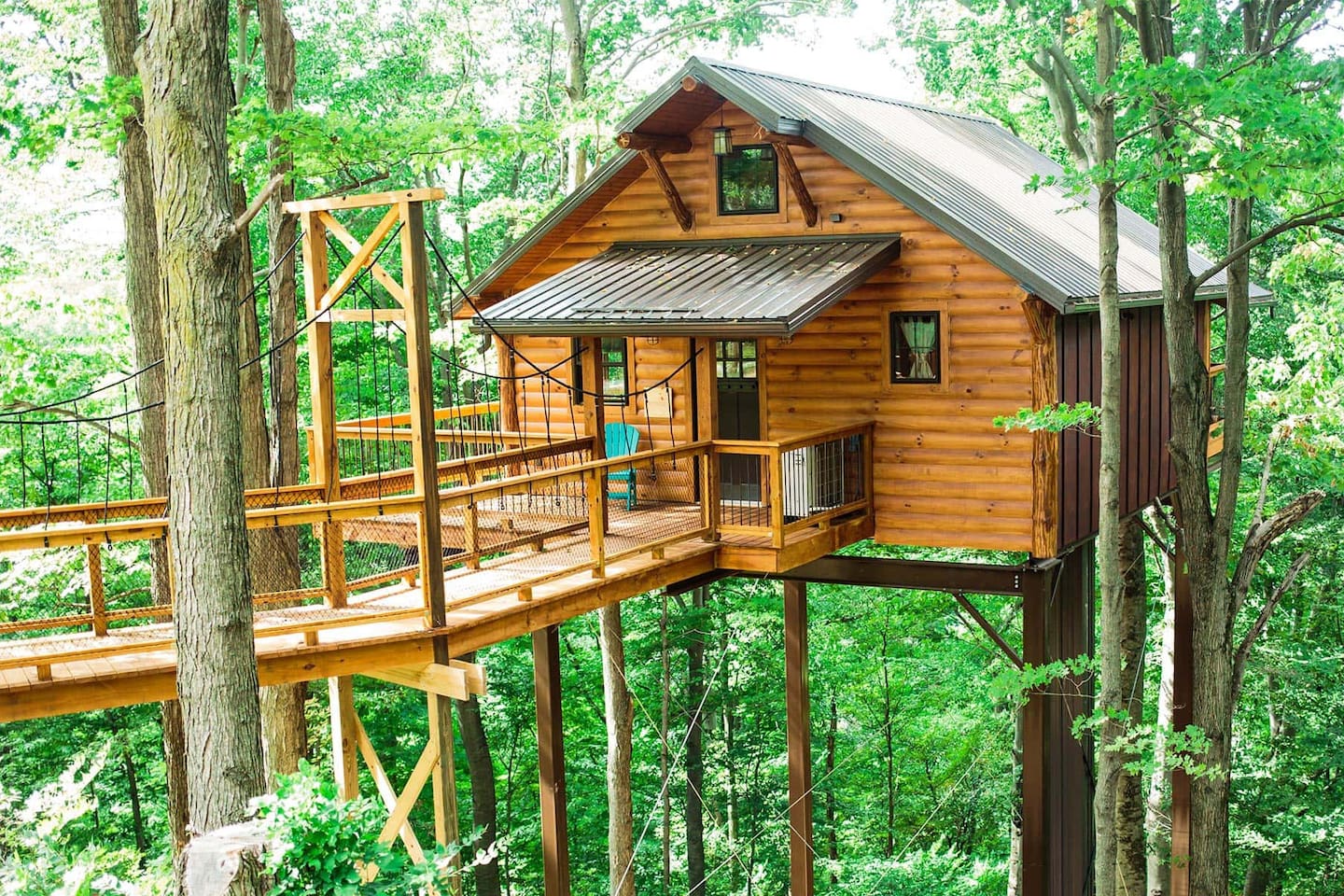 wooden cabin with bridge on stilts high in green trees