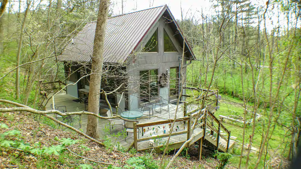 Rustic Hocking Hills Cabin with grey slate roof, and large wraparound deck, in wooded yard.
