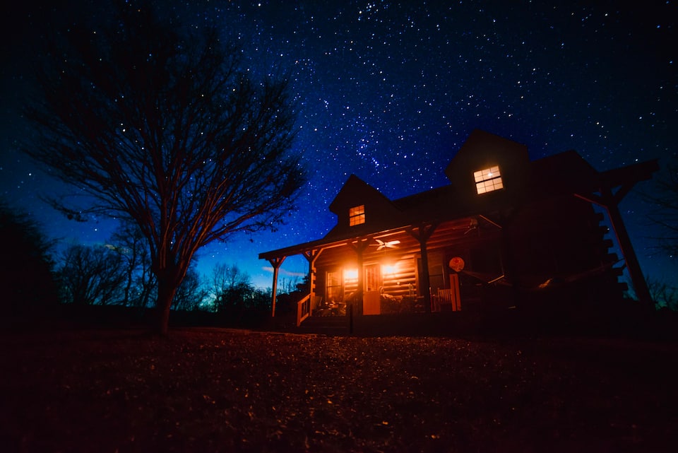 stunning photo of Virginia cabin at night with two front porch lights illuminated, against a bright starry sky.