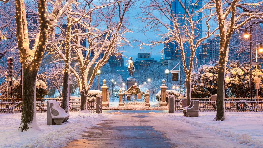 A walkway covered in snow surrounded by trees leading to a statue in Boston one of the Christmas vacations in the USA