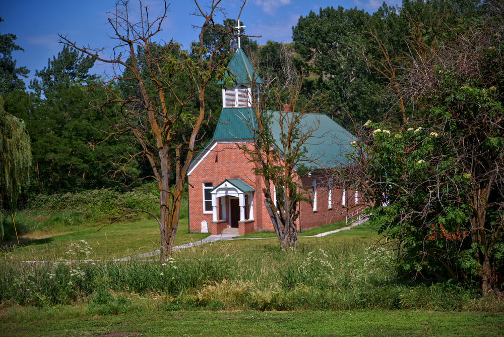 A church in the woods located in the Nez Perce national monument. The church is red brick with a green roof. 