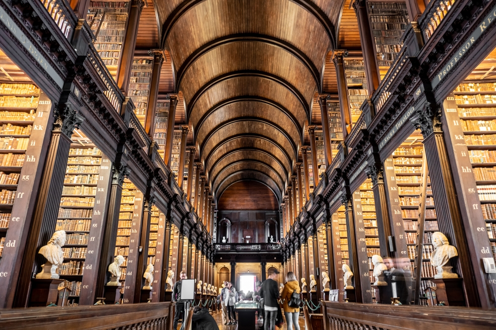 The Long Room in the Old Library at Trinity College Dublin. There are high book cases full of old books and statues around. 