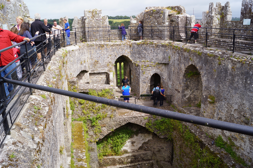 people inside a old castle with railings kiss the blarney stone