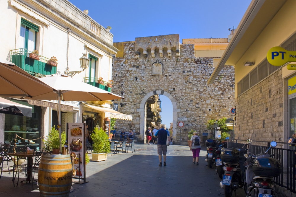 people walking towards an old brick gate things to do in taormina