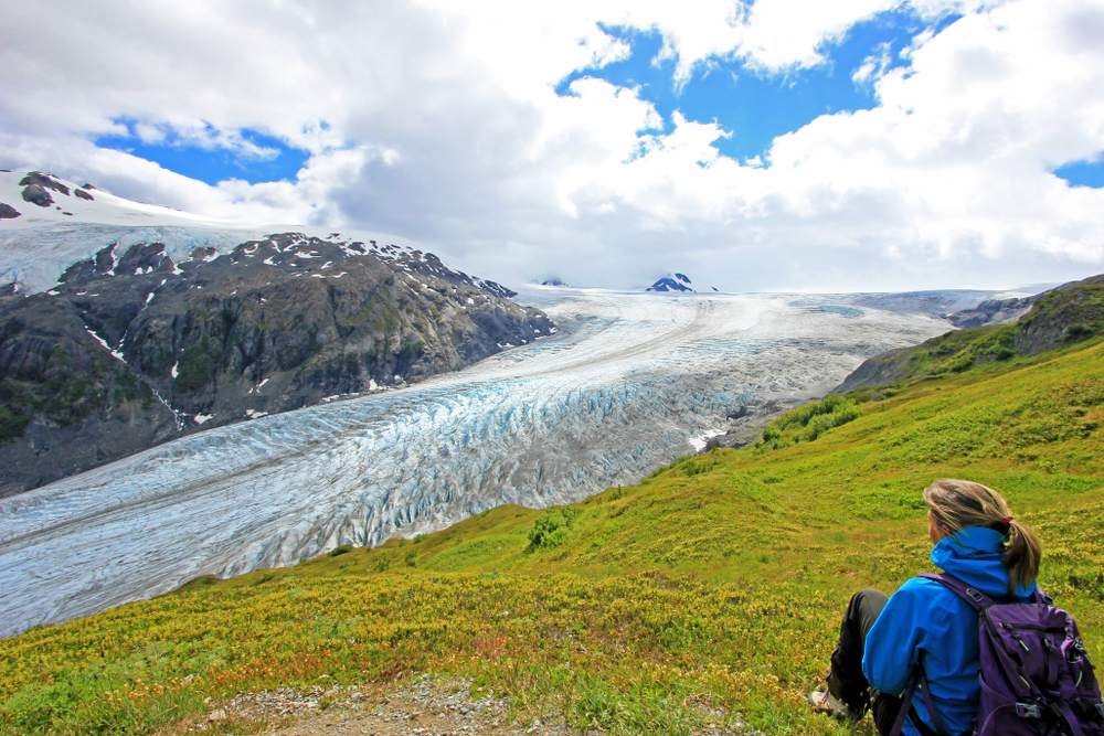 woman sitting on green grass and looking at the glacier 