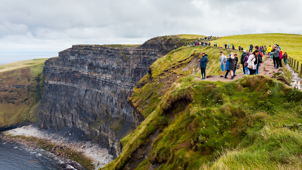 people standing on the edge of the cliffs of moher ireland