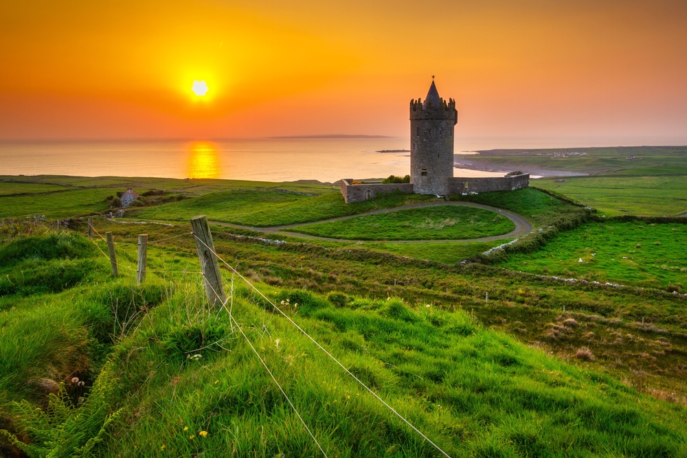 beautiful castle surrounded by green graas while the sun sets over the ocean