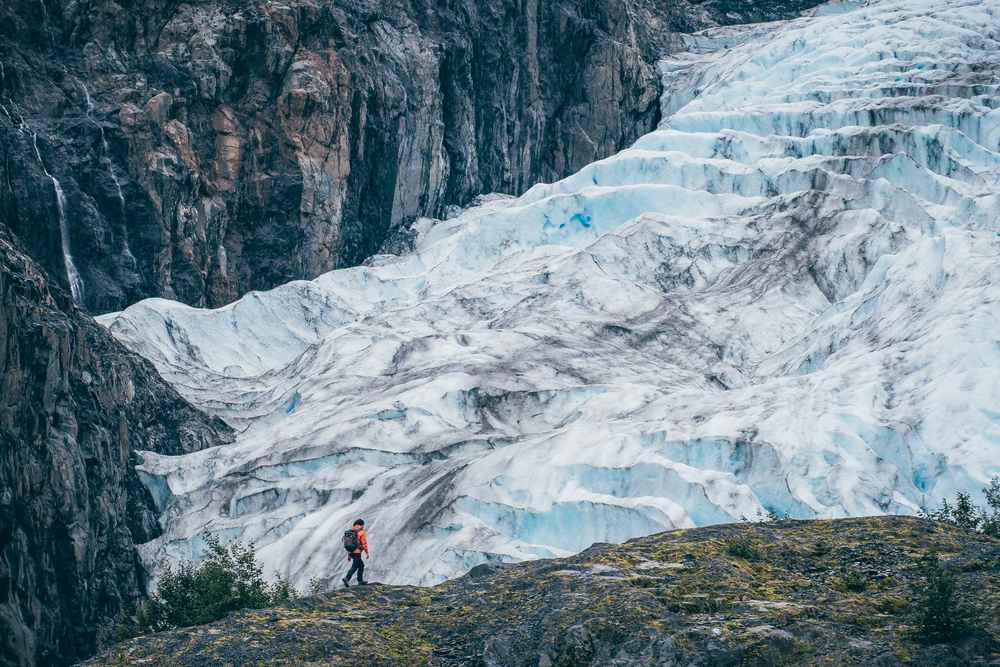 girl walking with a backpack in front of a glacier 
