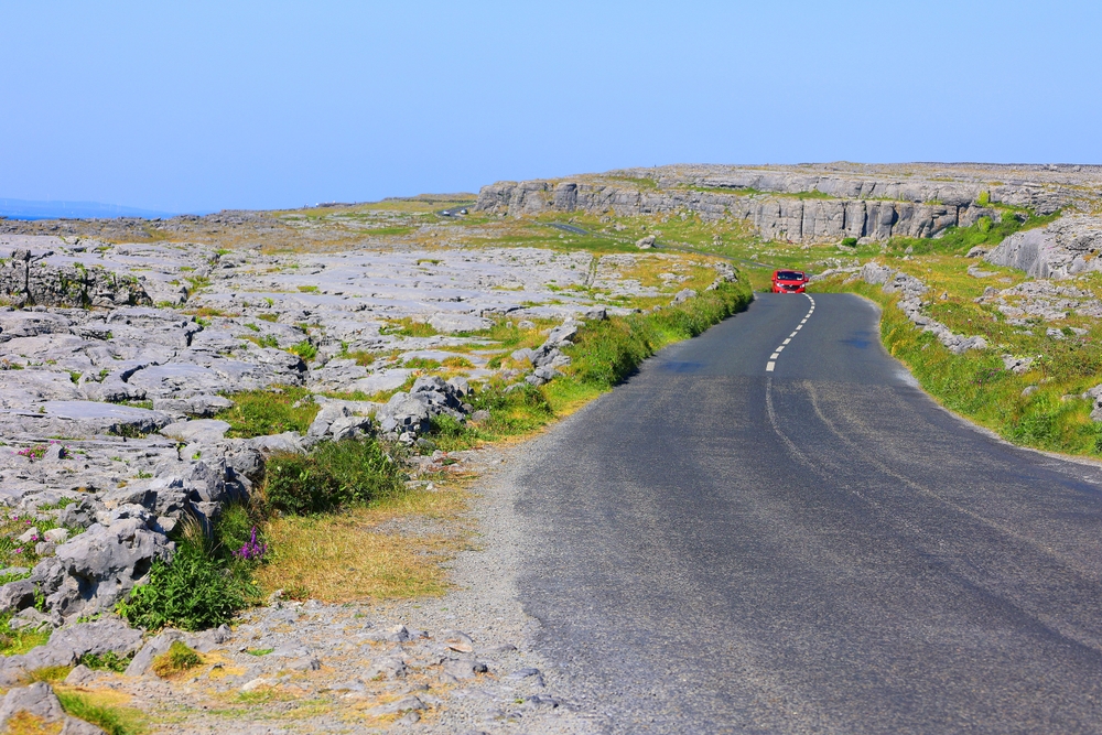 a red car driving on a road surrounded by rocks things to do in doolin