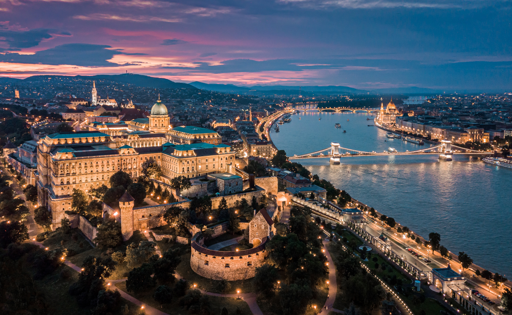aerial view of a city lit up at night beside a river with a bridge 2 days in budapest
