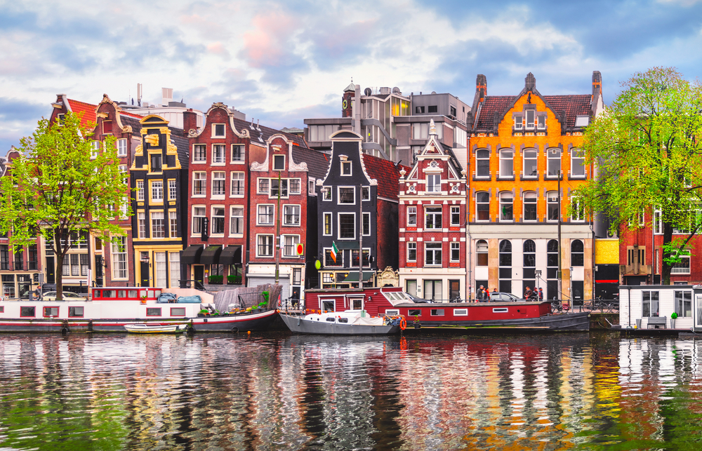 colorful houses and boats reflecting in water traveling to amsterdam