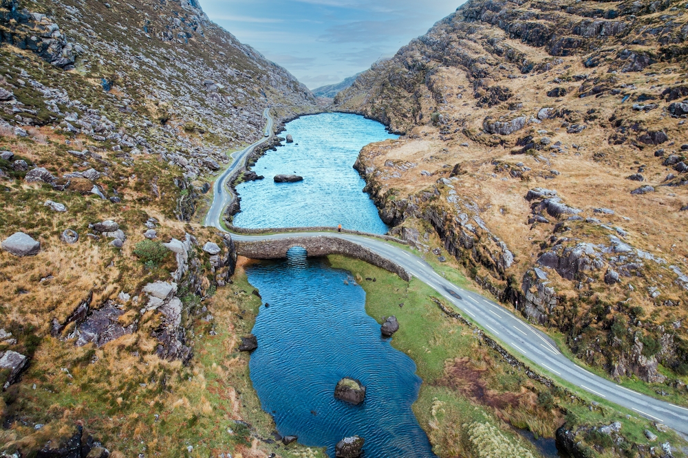 aerial view of a road over a lake surrounded by mountains traveling to ireland