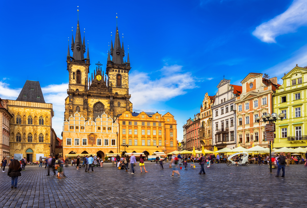 people walking around in a square surrounding by colorful and old buildings traveling to prague