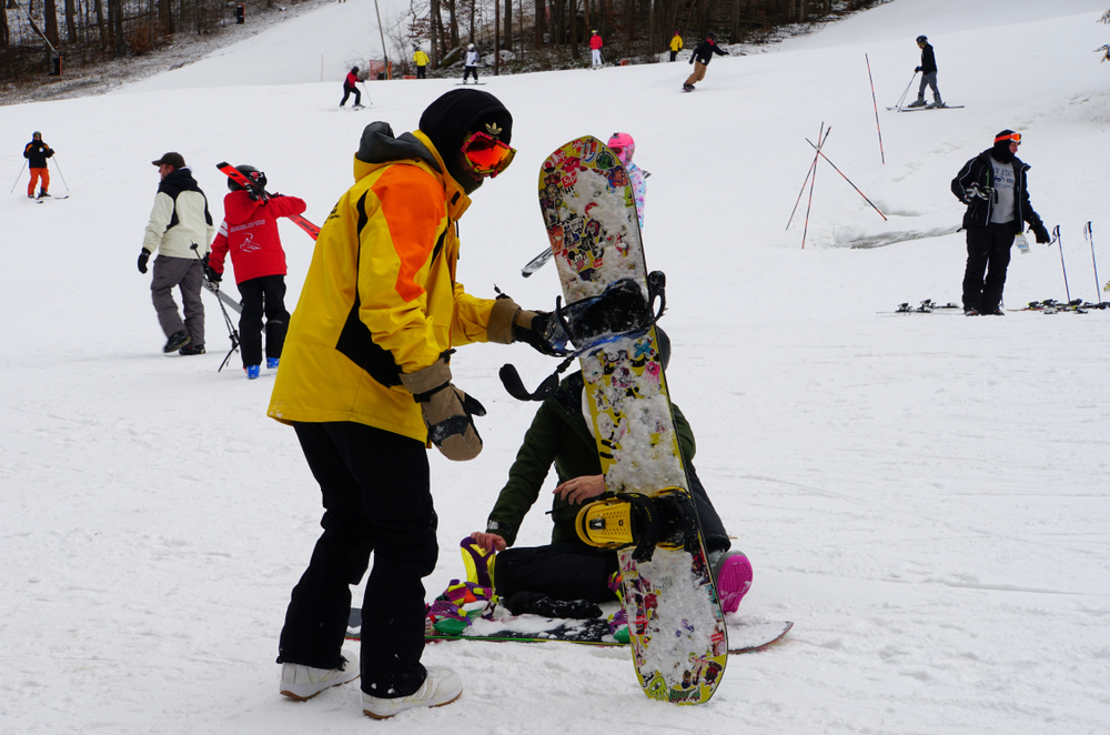 a man holding a snowboard with people skiing behind poconos in the winter