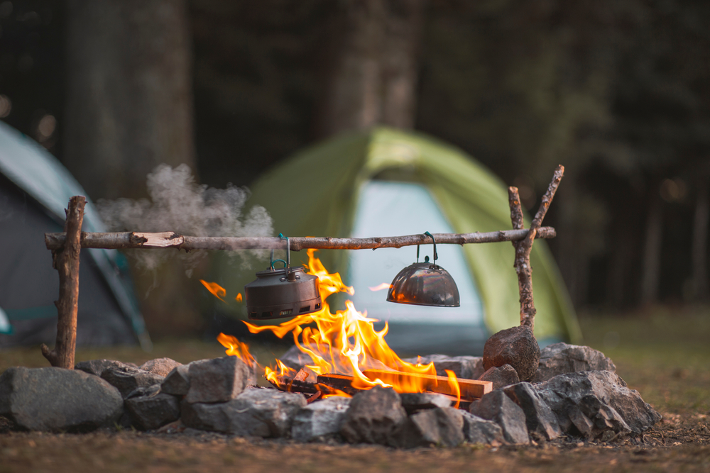 camp fire and tea pot in front of a green tent camping in the poconos