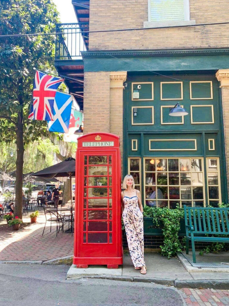 woman leaning on a red phonebooth in front of a cafe with different country flags hoisted