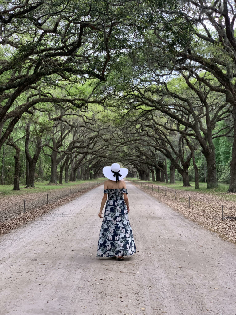 women in black long dress and white hat standing on a path surrounded by trees best things to do in savannah