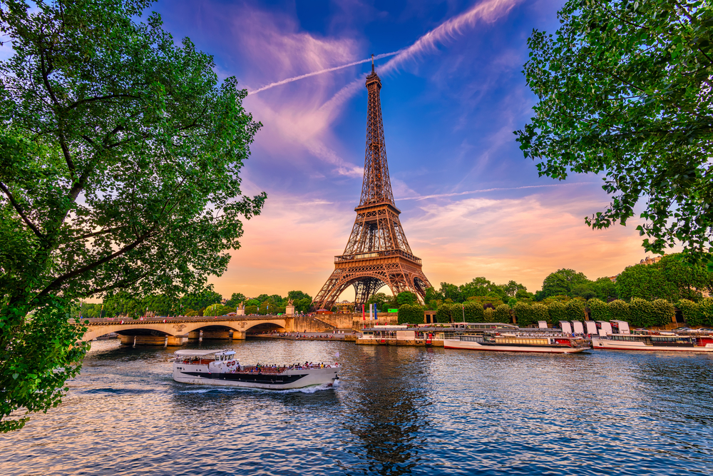 huge tower surrounded by trees and a river with a boat on it