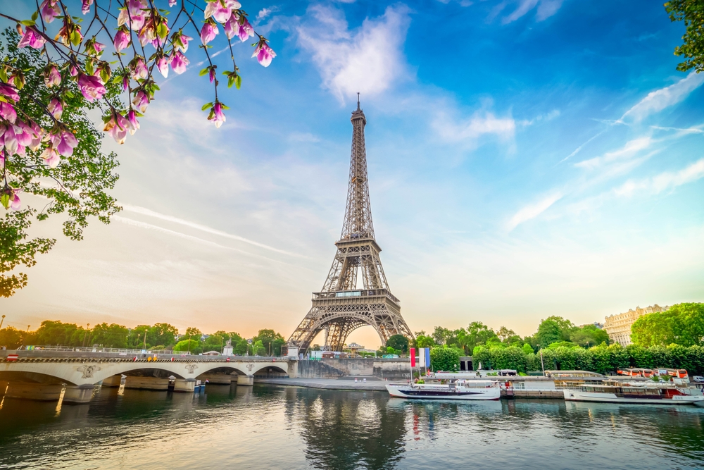 eiffel tower surrounded by trees with boats and river in front of it