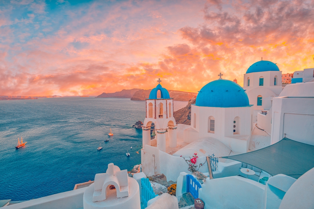 sunset over the blue domes of white buildings beside the ocean europe vacation tips