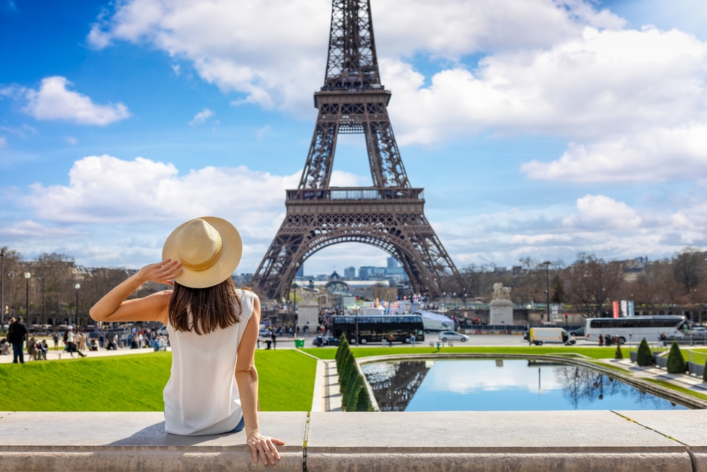 woman in white top and hat sitting and looking at eiffel tower