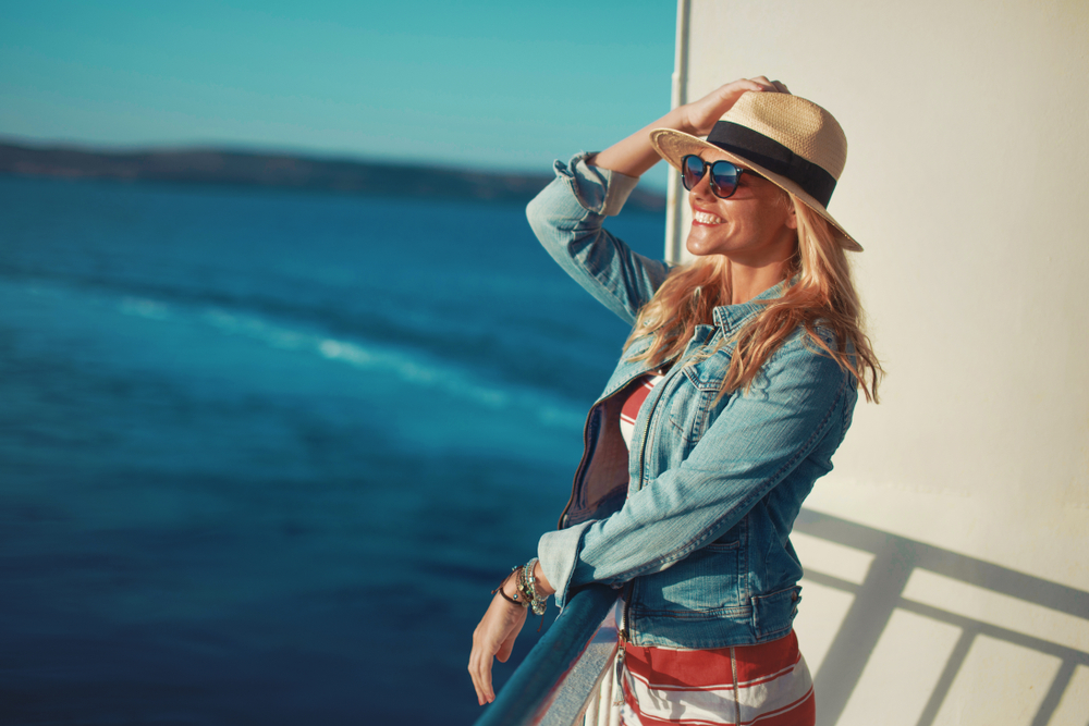 happy woman wearing a dress with a denim jacket, hat, and sunglasses