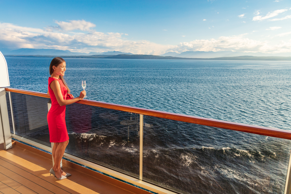 girl in red dress with a glass of champagne in hand standing on the deck mediterranean cruise packing list