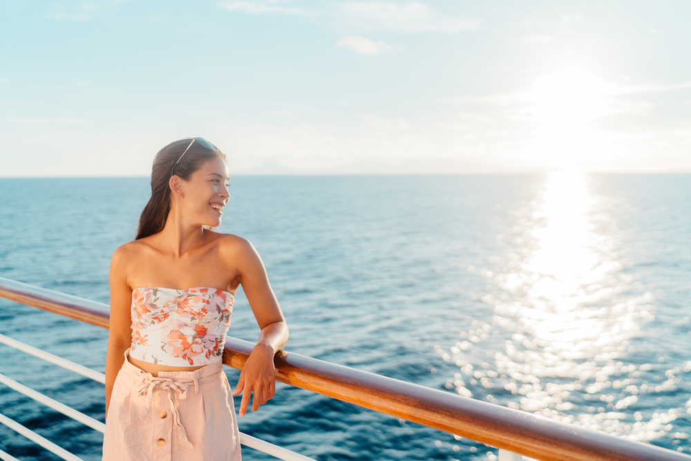 young woman smiling dressed up in cute top and shorts with sunglasses on the deck mediterranean cruise packing list