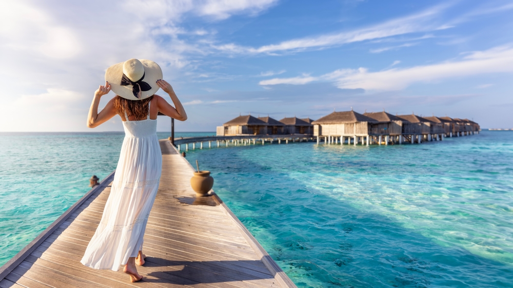 a woman in a white dress walking over a wooden bridge leading to the water villas