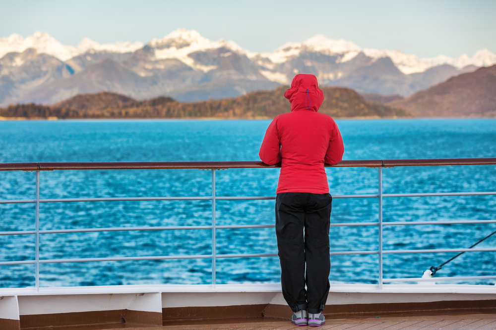 woman in red jacket and black pants watching the mountains on a cruise