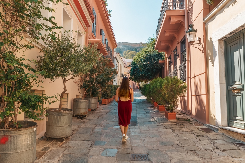a girl in a pink dress walking on a deserted street with lots of houses and plants