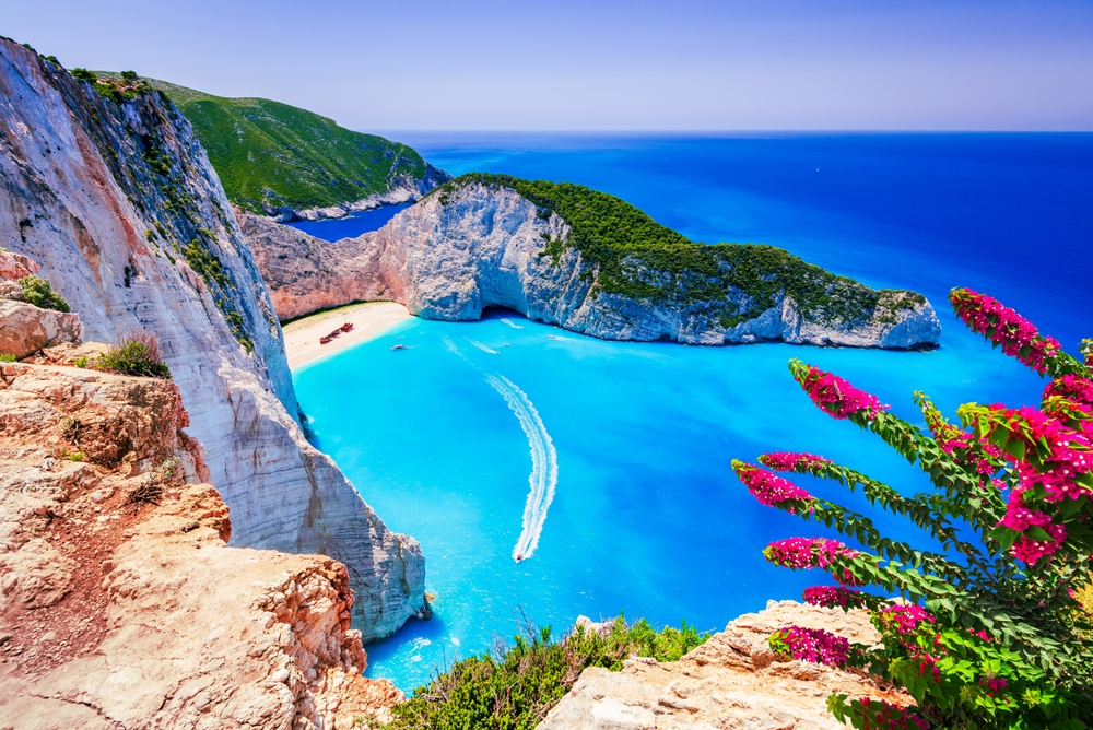 view from a cliff of a beach and blue lagoon surrounded by cliffs the greek islands
