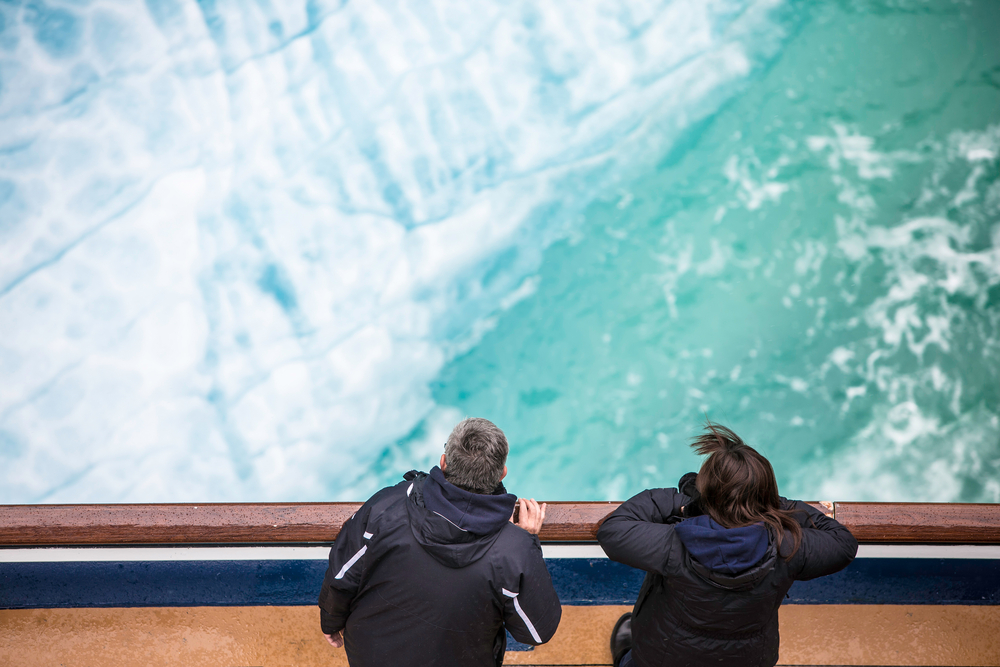 two passengers at ship railing looking at the glacier alaska cruise outfits for august