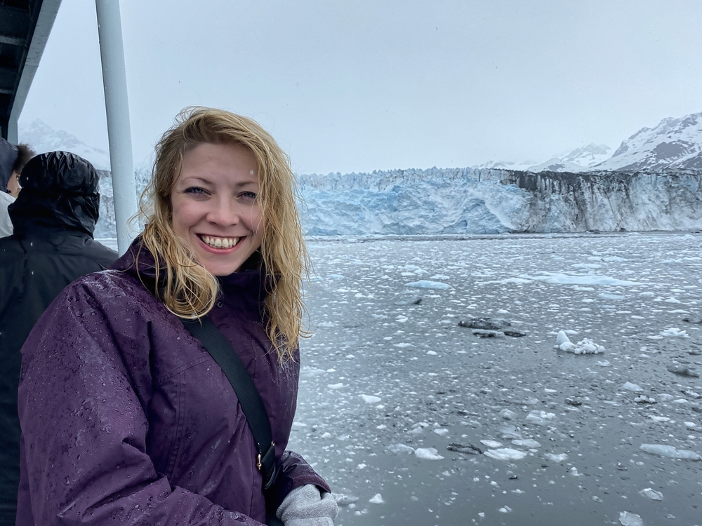 woman smiling into the camera with glacier behind her
