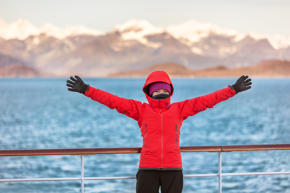 girl wearing orange jacket, black gloves, magenta cap, and a neck warmer on a cruise ship alaska cruise outfits for august