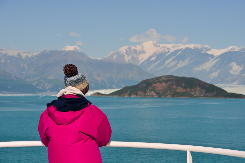 person in pink jacket looking at the snow covered mountains from a cruise ship alaska cruise outfits for august