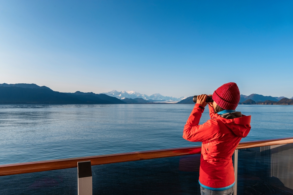 woman in orange jacket looking through binoculars
