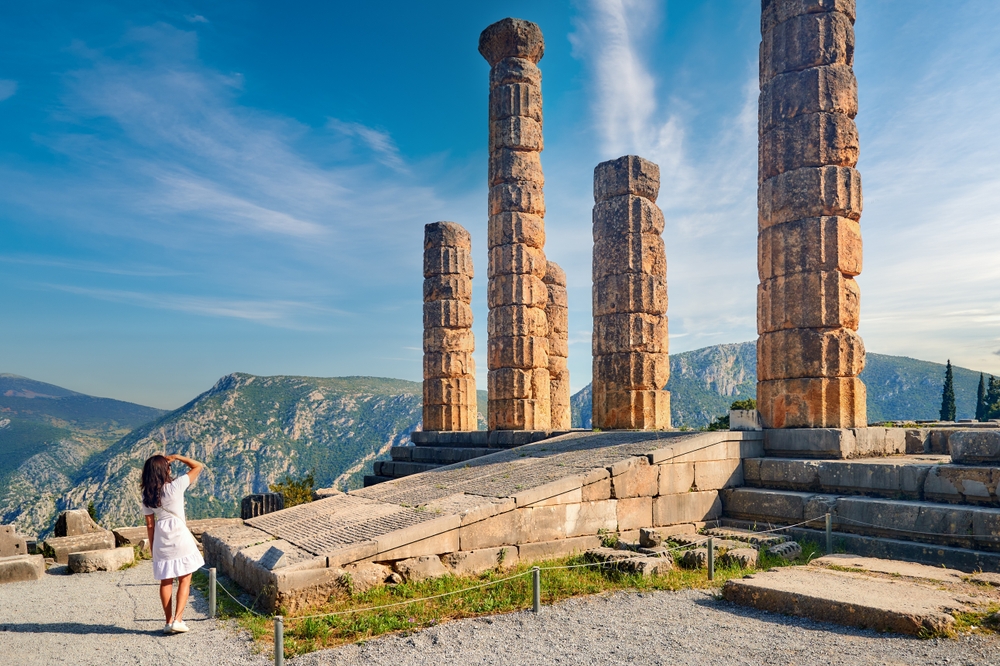 woman in white dress looking at big columns surrounded by mountains tours in athens