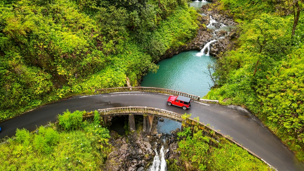 aerial view of a bridge with red car beside a waterfall and lots of trees warm weather getaways