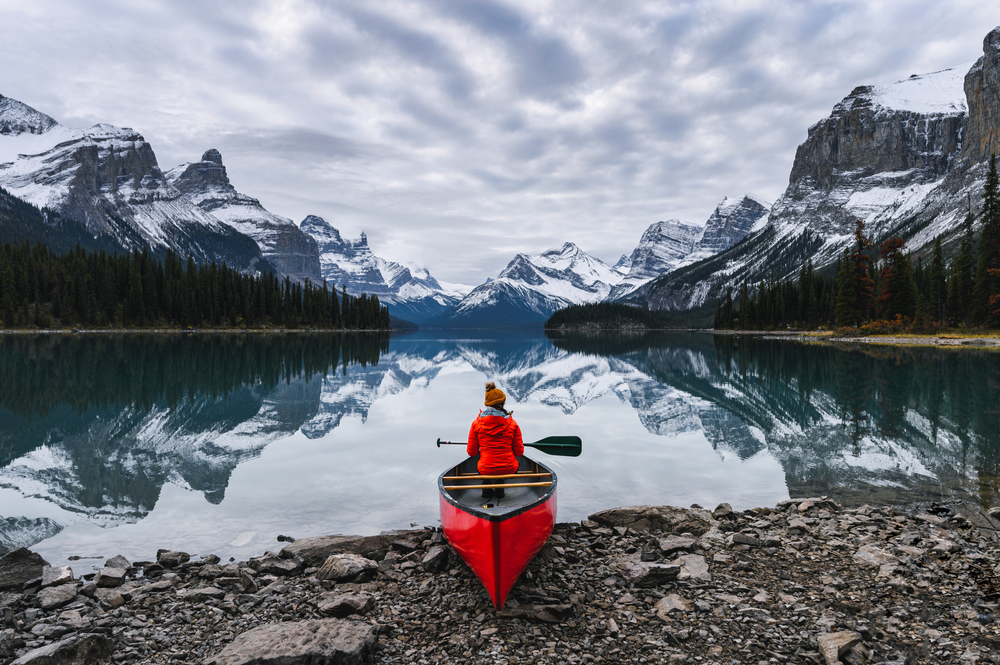traveler sitting with paddle on canoe in front of a lake reflecting mountains things to do in jasper