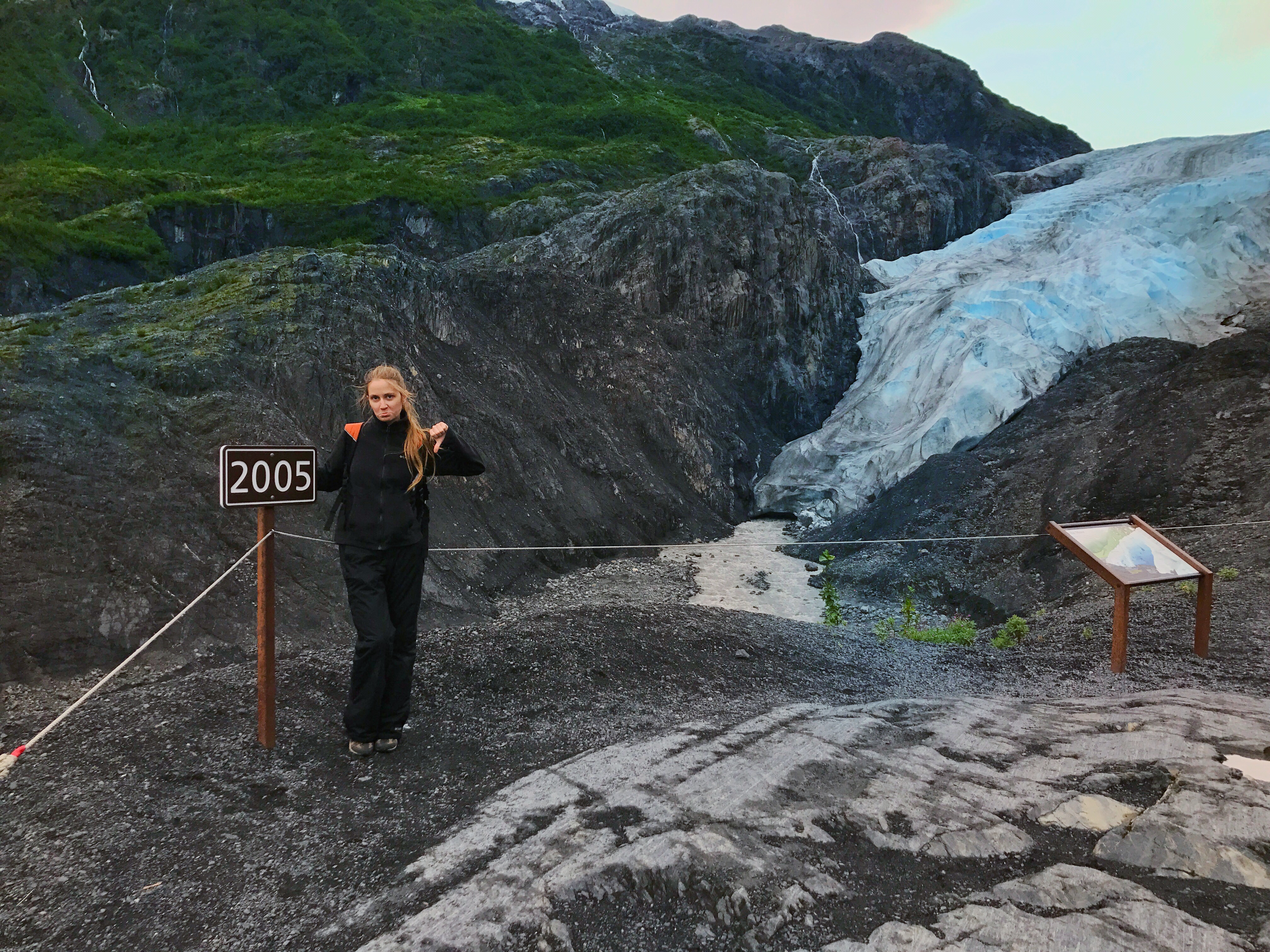 Unhappy Caucasian woman dressed in black with rocky outcroppings in background.