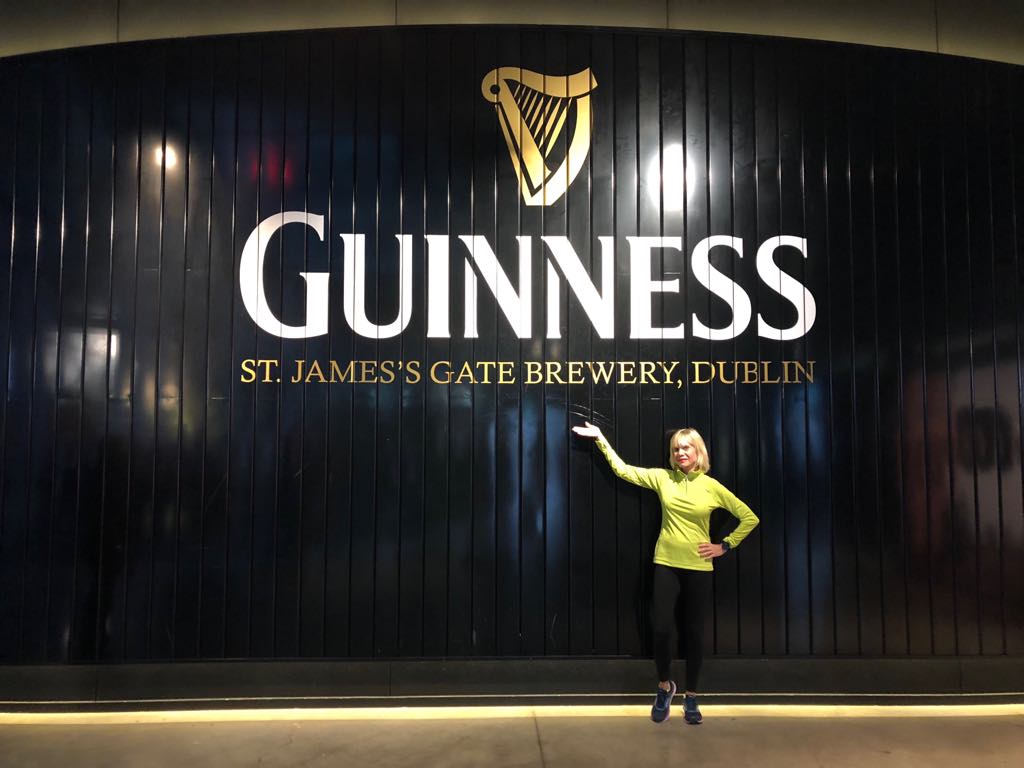 Woman waering yellow top pointing at the Guinness sign. 