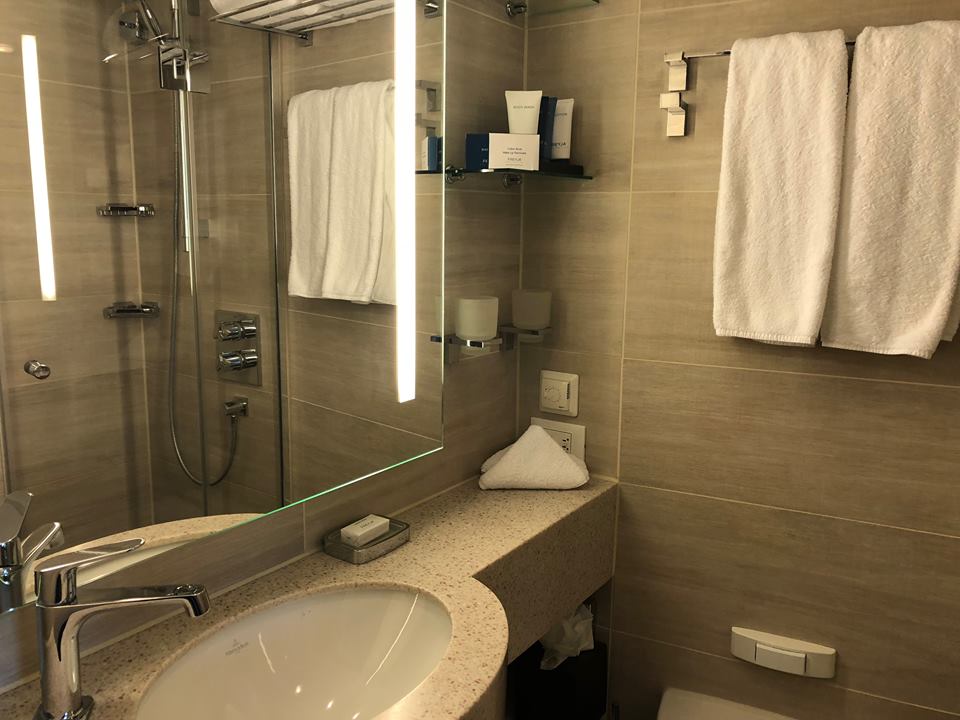 beige bathroom with white towels hanging and glass shower.