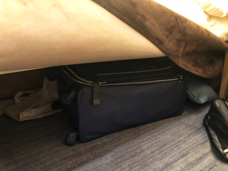 black suitcase under bed with beige and brown cover.