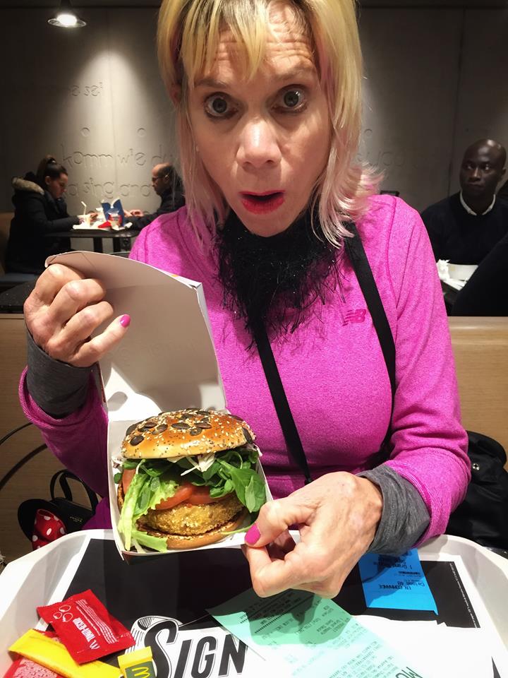 Caucasian woman with surprise on her face wearing pink top holding a McDonalds burger 