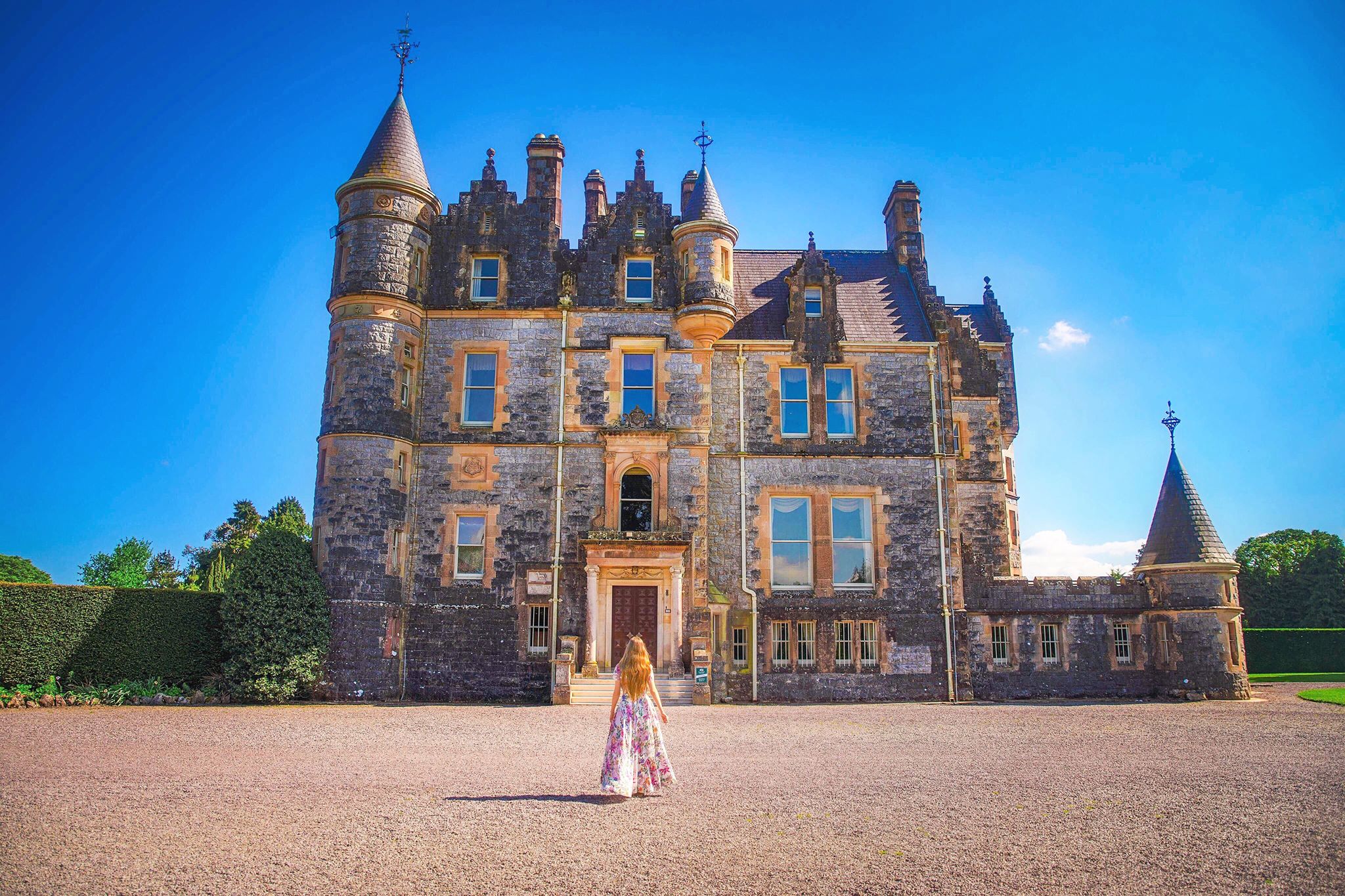 Kiss the Blarney Stone manor house with caucasian woman with flowing hair and flowering dress walking towards front door.