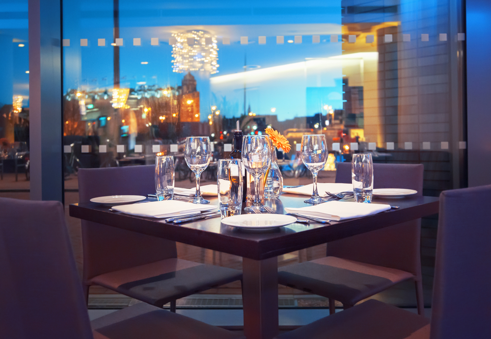 Plates and glasses set on a table at a restaurant with views of the city.