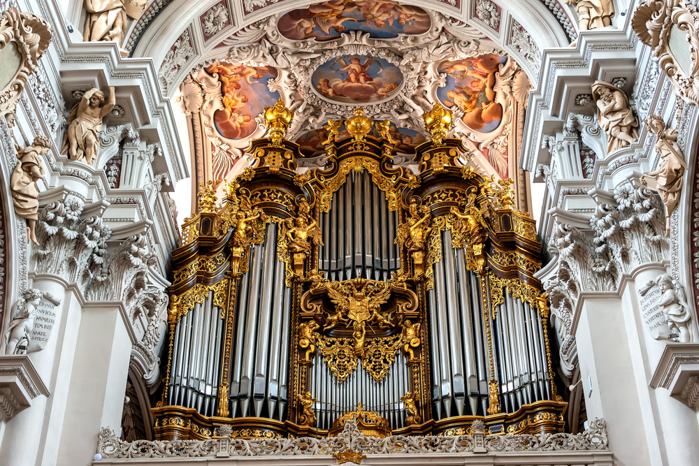 The intricate St. Stephen Cathedral organ with gold details and a painted ceiling above it with sculptures around it.