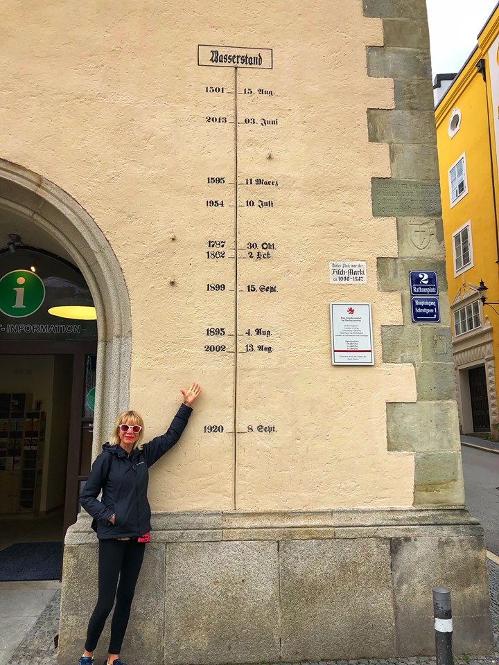 Blonde woman standing next to the marked water levels on the Passau town hall.