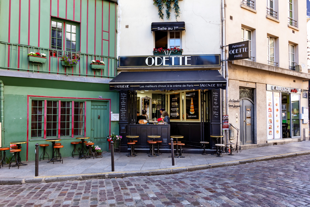 Unusual things to do in Paris Odette pastry shop with green fasade, cute tables and chairs with cobblestone road in foreground